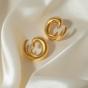 Macro shot of gold spiral shell earrings on elegant white satin background fabric