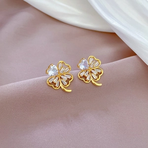 Macro detail of gold clover stud earring with white zircon inlay on soft silk fabric