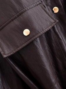 Detail of dark brown faux leather texture featuring a pocket flap and a gold metal button