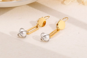 Close-up of geometric Saturn pearl earrings in polished gold and silver plated steel