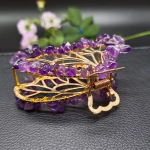 Golden butterfly hair claw with natural purple crystal stones on black leather background