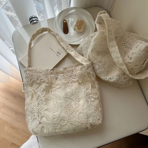 Close-up of beige lace embroidery handbag showing floral pattern and brand woven label