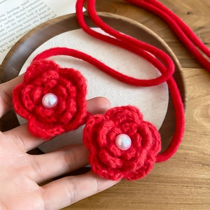 Detailed close-up of handmade red crochet flower necklace with central pearl on wood