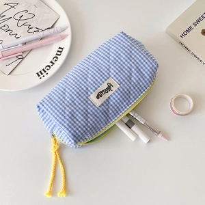 Close-up of quilted blue plaid stationery pouch with a yellow zipper pull on a white desk
