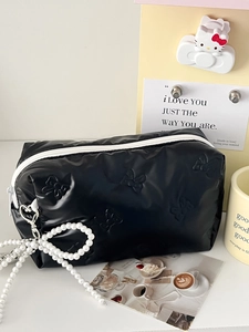 Quilted black cosmetic bag with bow patterns, pearl charm, and white zipper closure