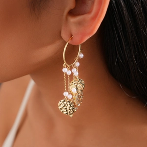 Close-up of model wearing gold hoop earrings with white pearls and metal disc tassels