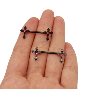 Detailed view of black cross nipple rings with red teardrop gems held in hand