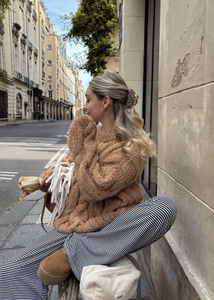 Close-up of brown chunky cable knit sweater texture and fabric details on urban street