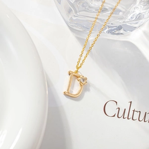 Detail of gold letter D pendant necklace with a small floral zircon accent and O-chain