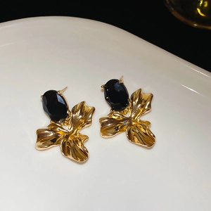 Close-up of golden petal earrings with oval black stones on a white ceramic plate