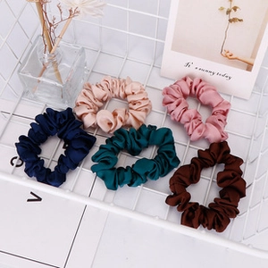 Detailed view of checkered silk scrunchies in five colors inside a white wire basket