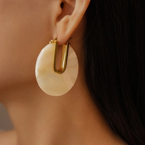 Close-up of 18k gold-plated U-shaped earrings with white marble resin discs on model