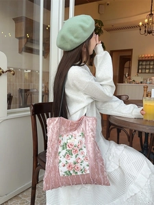 Chic pink velvet tote bag with rose floral embroidery shown in a warm cafe setting