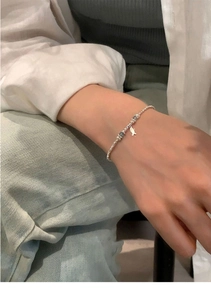 Close-up of pearl and silver bead bracelet with blue accent and small fish charm on wrist