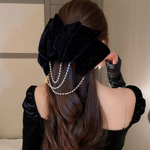 Detail of black velvet bow hair clip with layered pearl tassels on long hair