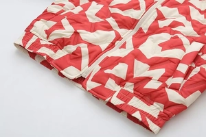 Détail de veste géométrique rouge et crème montrant le zip en métal et l'ourlet élastique