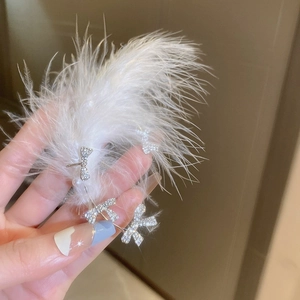 Detail shot of silver bow earring with rhinestones resting on soft white feathers