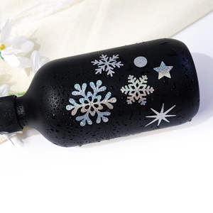 Detail of holographic snowflake stickers on a matte black bottle with water droplets