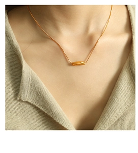 Close-up of minimalist gold twisted cylinder pendant necklace on a female model neck