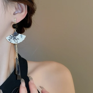 Détail de boucles d'oreilles à pompon et motif éventail en bambou portées sur un modèle
