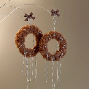 Close-up of brown plush circle earrings with silver bead chain tassels and bow detail