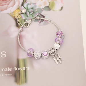 Silver charm bracelet with purple crystals and dreamcatcher pendant on floral backdrop