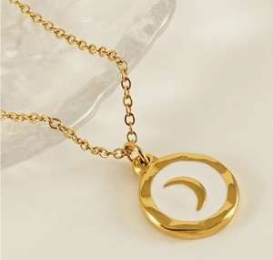 Close-up of golden necklace with white enamel moon pendant detail and polished finish