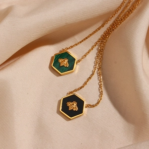 Close-up of gold bee pendants on green and black hexagonal bases over silk fabric
