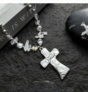 Detail of cross pendant with fish relief on crystal beaded necklace over black rock