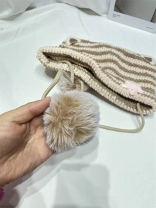 Detail of striped knit cat ear hat with a fluffy faux fur pompom and sequin star patch