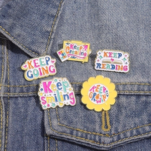 Detailed view of colorful enamel pins with inspirational quotes on denim jacket