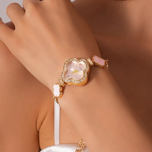 Detailed close-up of a gold clover watch with diamond-encrusted pink dial on model's wrist