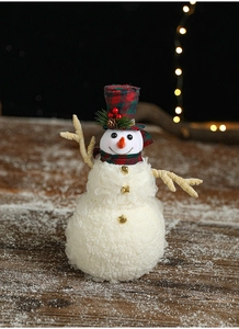 Detail of plush snowman with red-green plaid hat, carrot nose and bells on wood surface