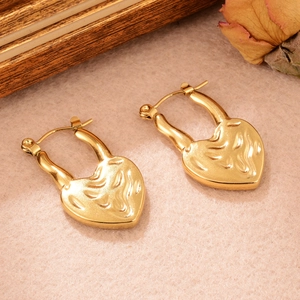 Détail de boucles d'oreilles créoles cœur dorées sur fond vintage avec texture