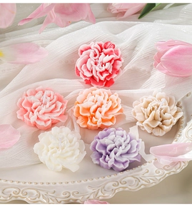 Detail of six colorful carnation-shaped soy wax candles on a white embossed decorative plate