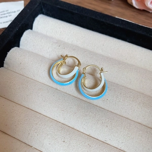 Close-up of gold-plated double hoop earrings with blue and white enamel inlay