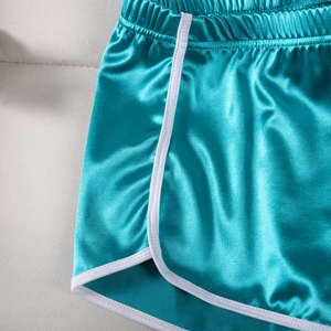 Detailed macro view of the satin turquoise fabric and white contrast trim of the shorts