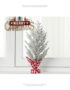 Close-up of mini snow-flocked Christmas tree with red-white plaid base and wooden sign