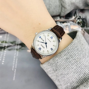 Women's watch with small white dial, Roman numerals, and brown leather strap on wrist