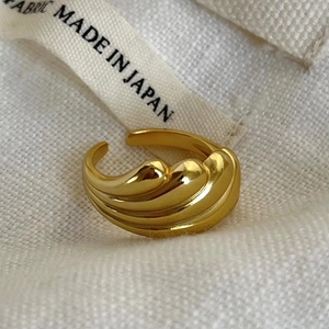 Minimalist gold wavy open ring featuring smooth metallic texture on textured white fabric