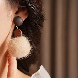 Detail view of retro earrings with dark wood circle and beige plush ball on a model