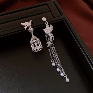 Detailed close-up of asymmetrical birdcage and pearl tassel earrings on black tray