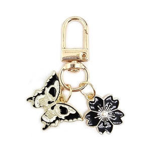 Detail view of a black and white skull butterfly and sakura charm on a gold metal keychain
