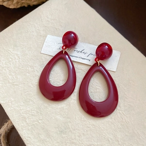 Macro detail of wine red resin teardrop earrings on a beige textured paper background