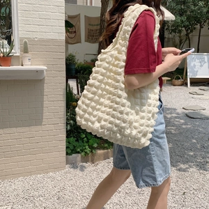 Outdoor shot of a cream bubble textured cloud tote bag worn on a woman's shoulder