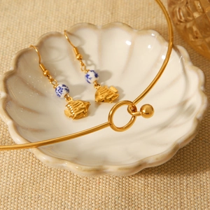 Macro detail of a gold ocean style necklace and ceramic earrings in a shell-shaped dish