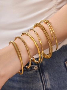 Detail of stacked gold bamboo joint and spiral bangles worn on a model's wrist