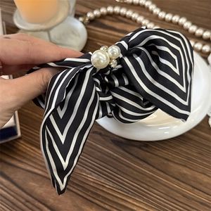 Detail of a black and white striped bow hair tie with pearls and satin fabric texture