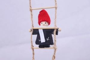 Detail of wool felt Christmas gnome with wood beads climbing a natural jute rope ladder