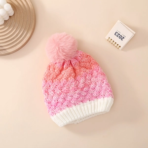 Detail of pink and white gradient knit winter hat featuring a fluffy faux fur pompom